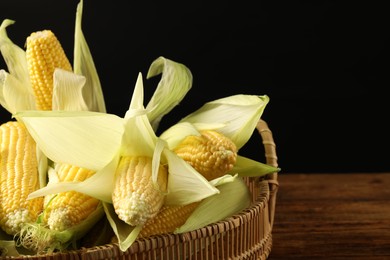 Photo of Many fresh ripe corncobs with green husks on wooden table, closeup. Space for text