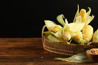 Photo of Many fresh ripe corncobs with green husks and kernels on wooden table. Space for text