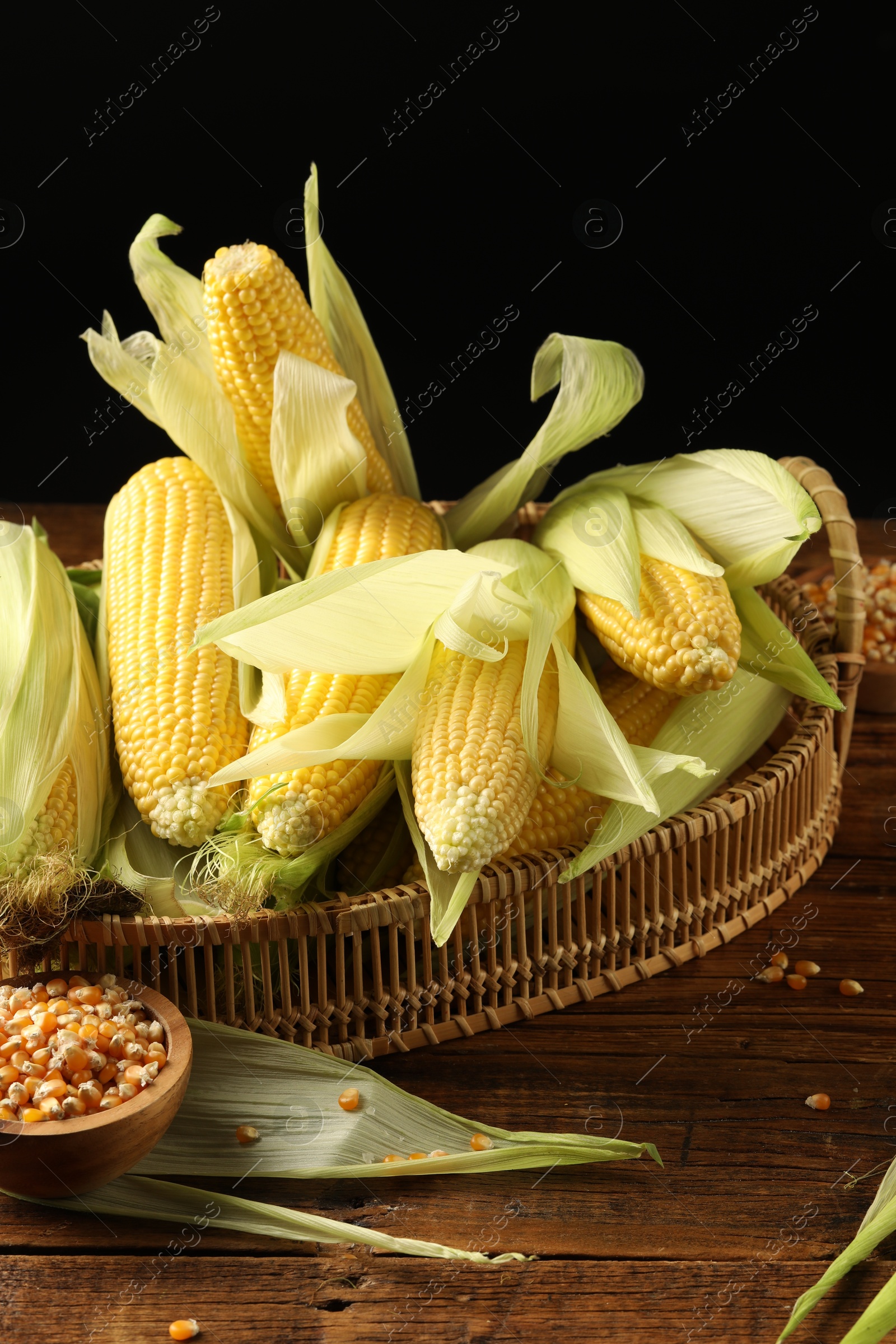 Photo of Many fresh ripe corncobs with green husks and kernels on wooden table