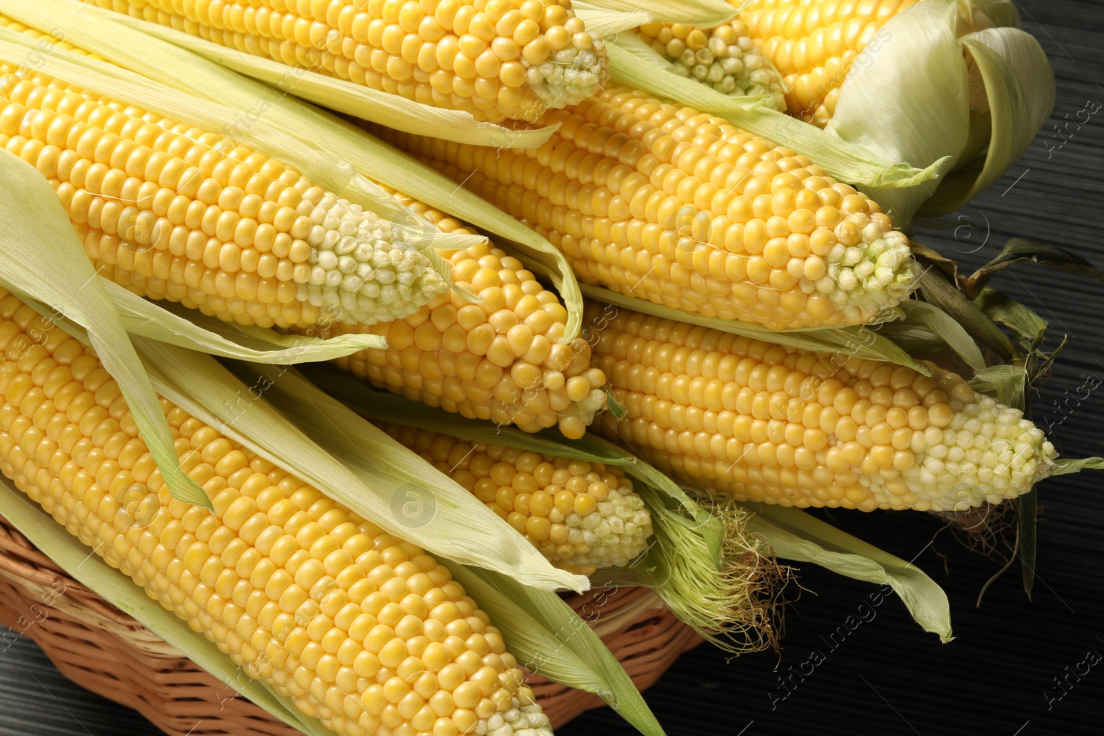 Photo of Many fresh ripe corncobs with green husks on wooden table, closeup