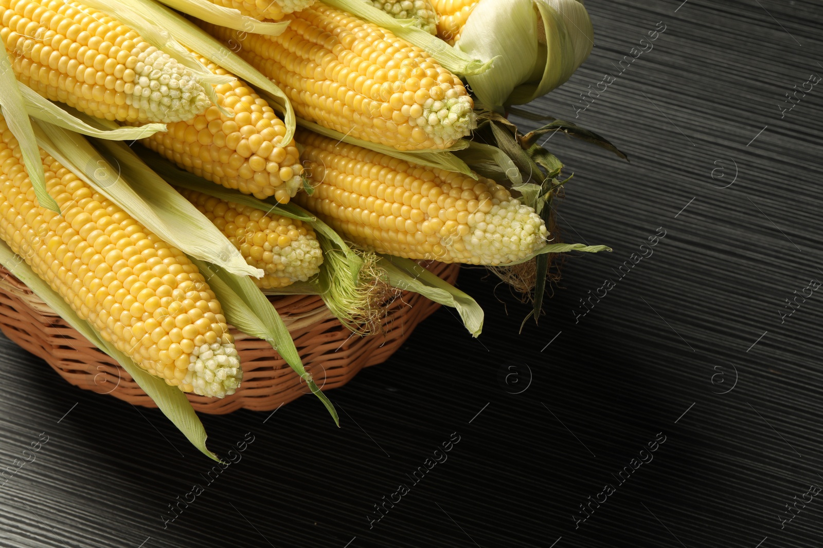 Photo of Many fresh ripe corncobs with green husks on wooden table, closeup. Space for text