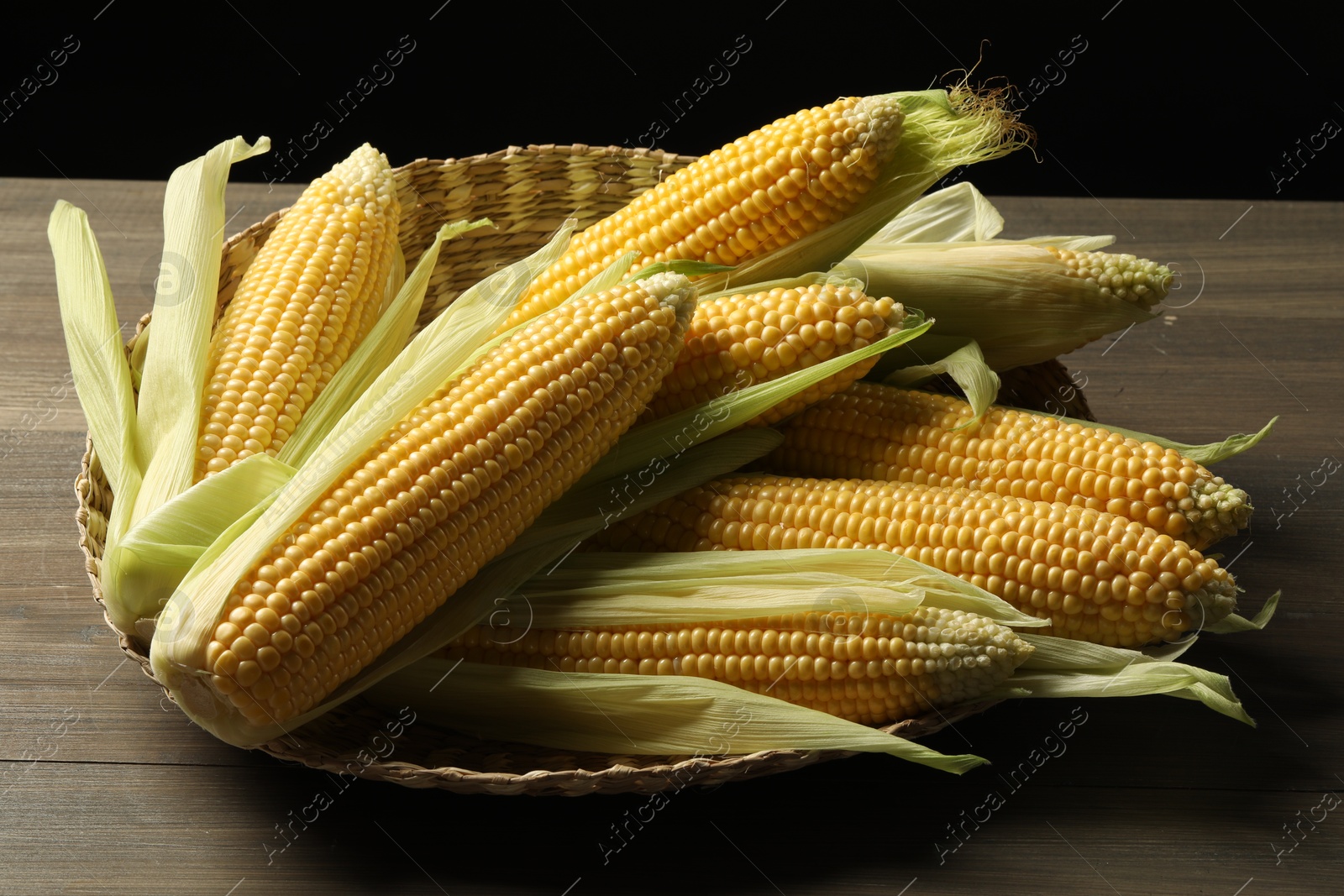 Photo of Many fresh ripe corncobs with green husks on wooden table