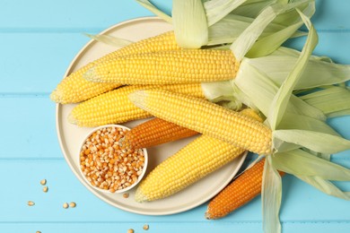 Photo of Many corncobs and kernels on light blue wooden table, top view