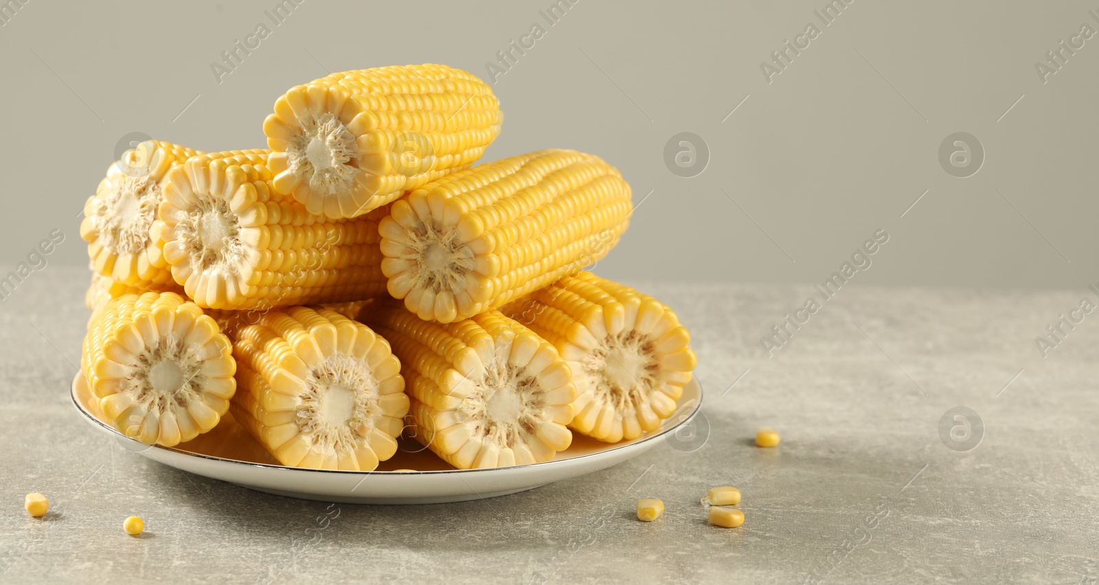 Photo of Halves of fresh ripe corncobs on grey table. Space for text