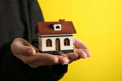 Photo of Woman with house model on yellow background, closeup