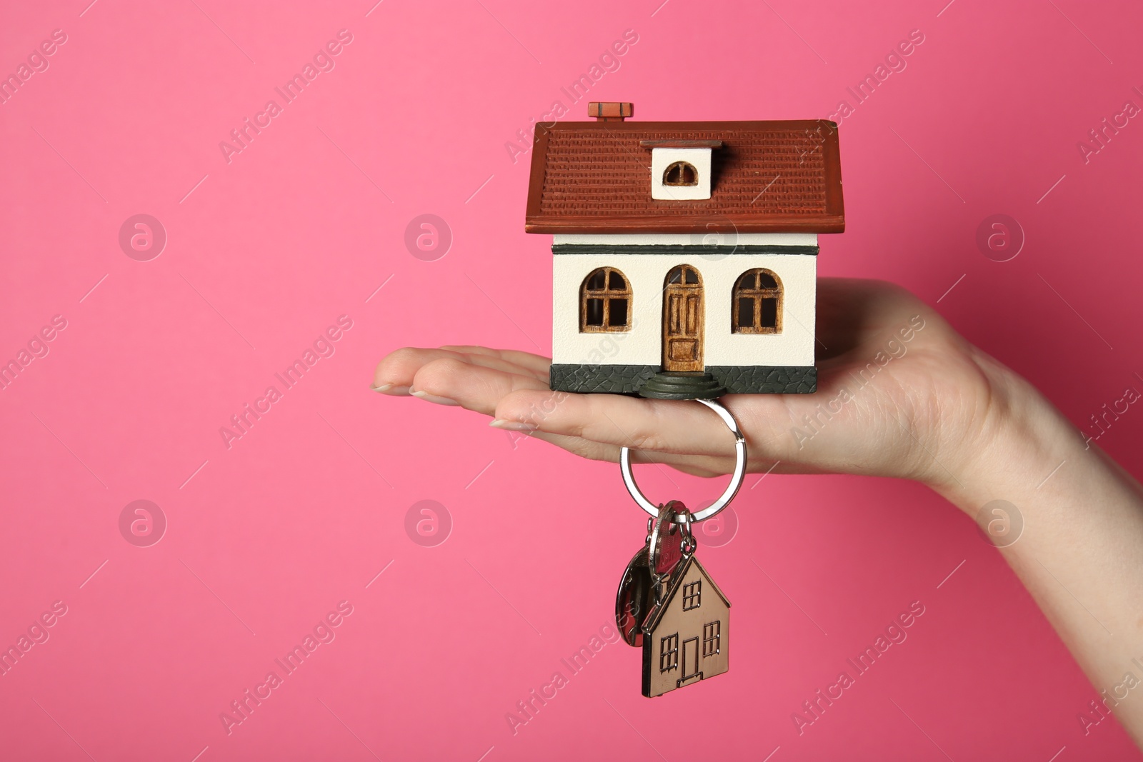 Photo of Woman with house model and key on pink background, closeup. Space for text