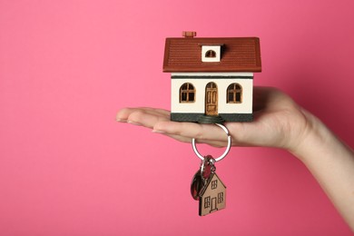 Photo of Woman with house model and key on pink background, closeup. Space for text