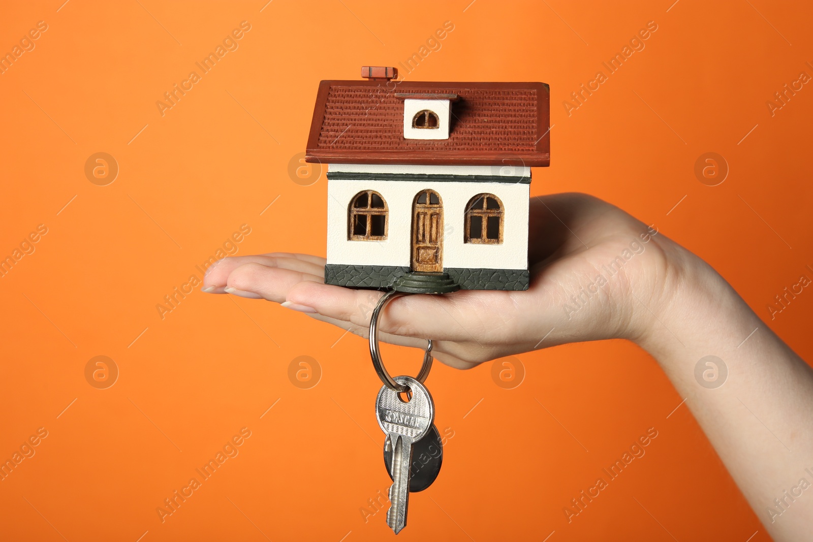 Photo of Woman with house model and key on orange background, closeup