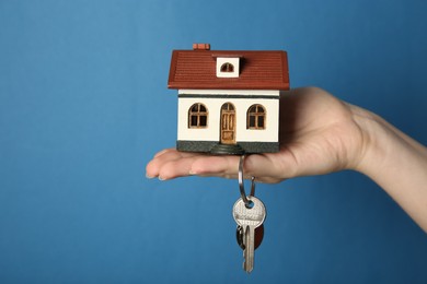 Woman with house model and key on light blue background, closeup