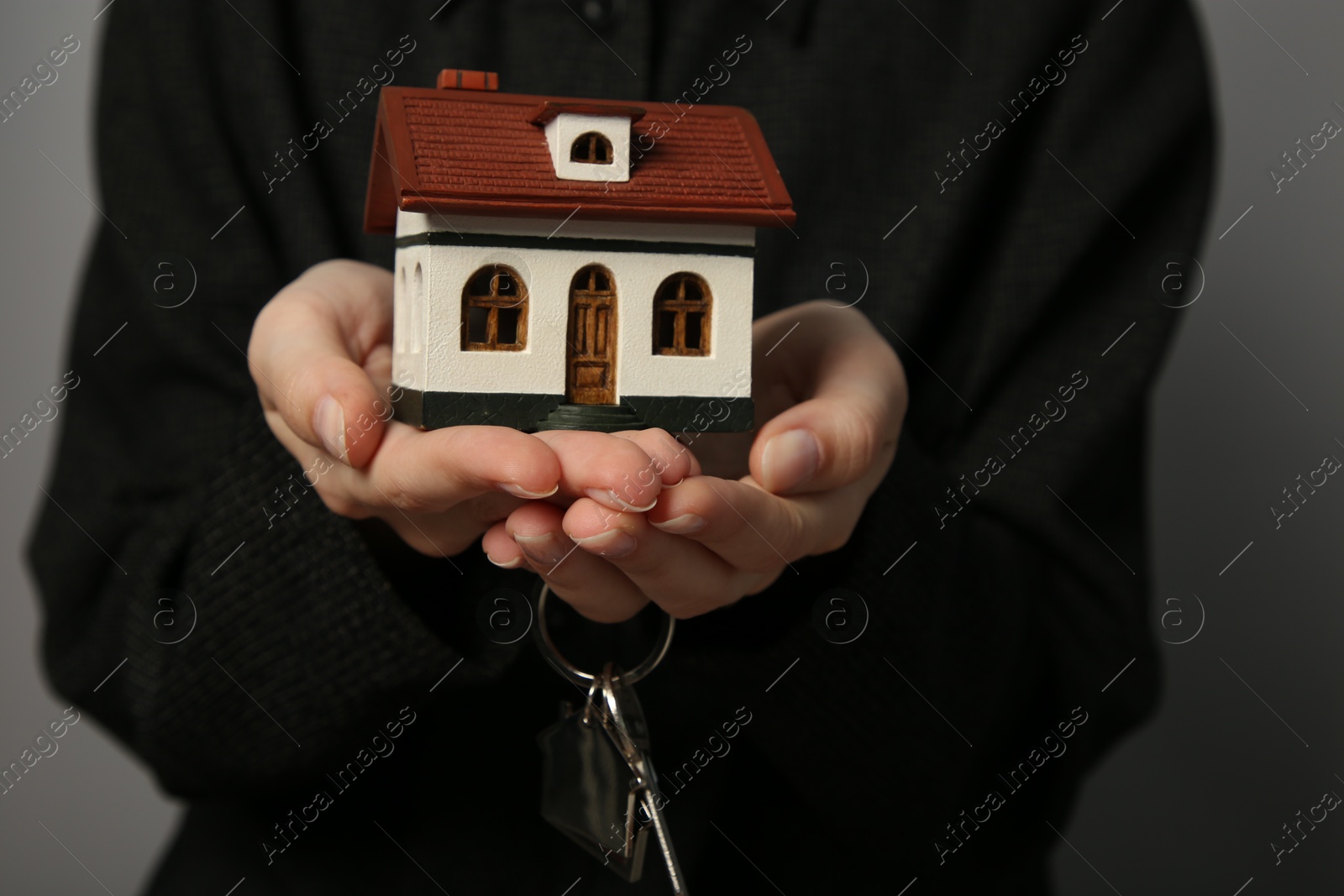 Photo of Woman with house model and key on grey background, closeup