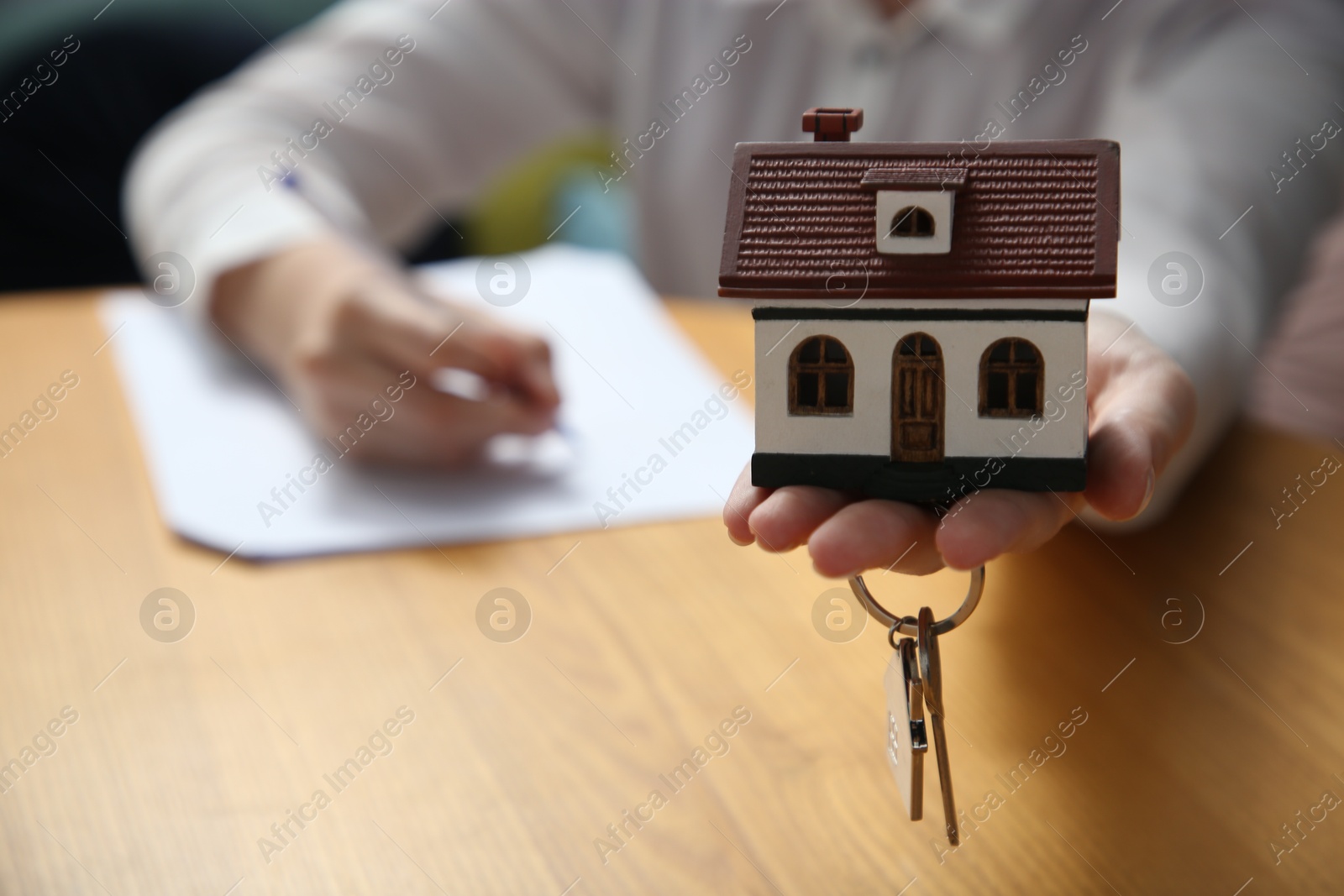 Photo of Woman working with document while holding house model and key at wooden table indoors, closeup