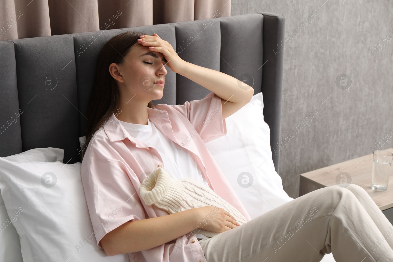 Photo of Woman using hot water bottle to relieve menstrual pain on bed at home