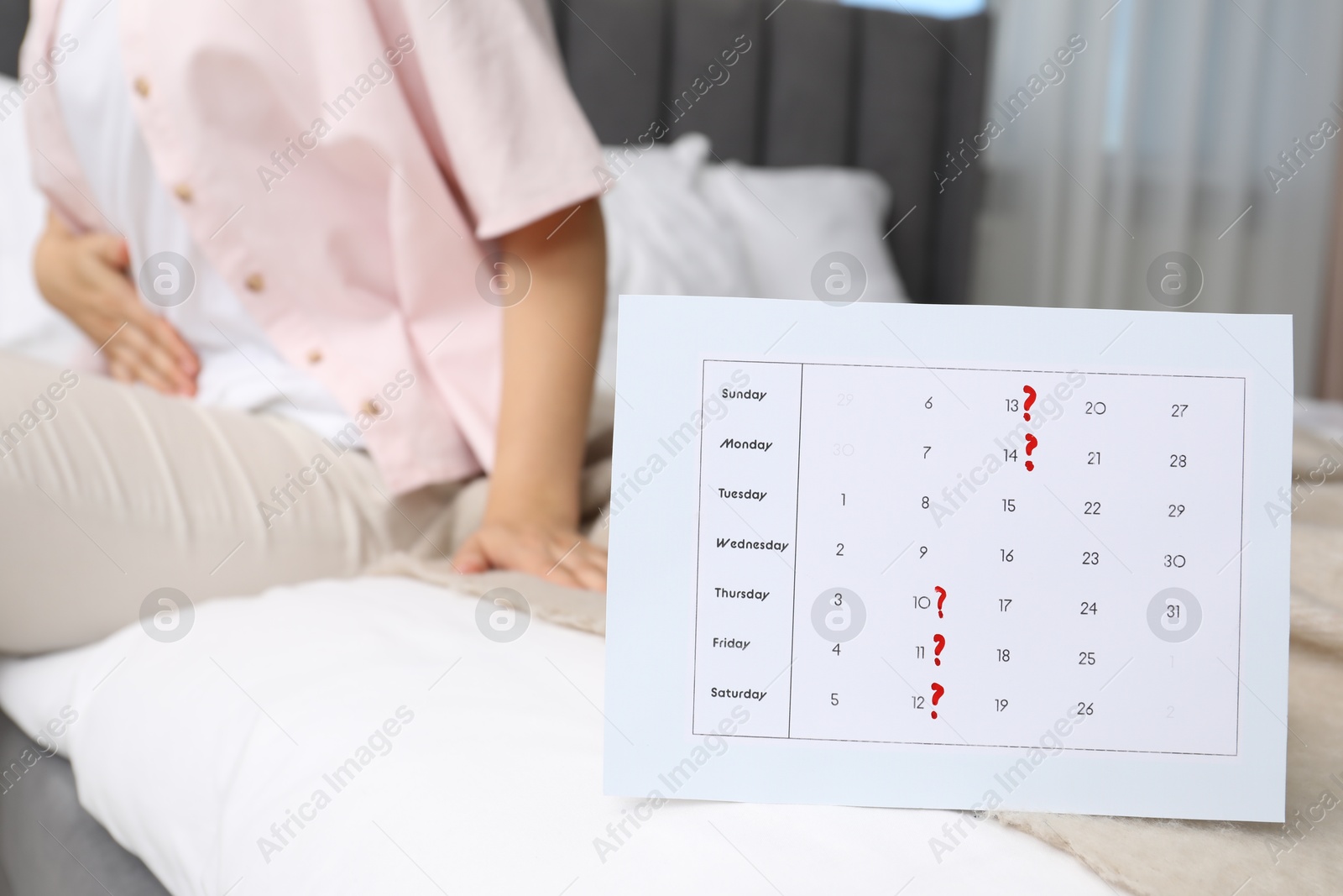 Photo of Woman suffering from abdominal pain in bed at home, focus on calendar with marked menstrual cycle days