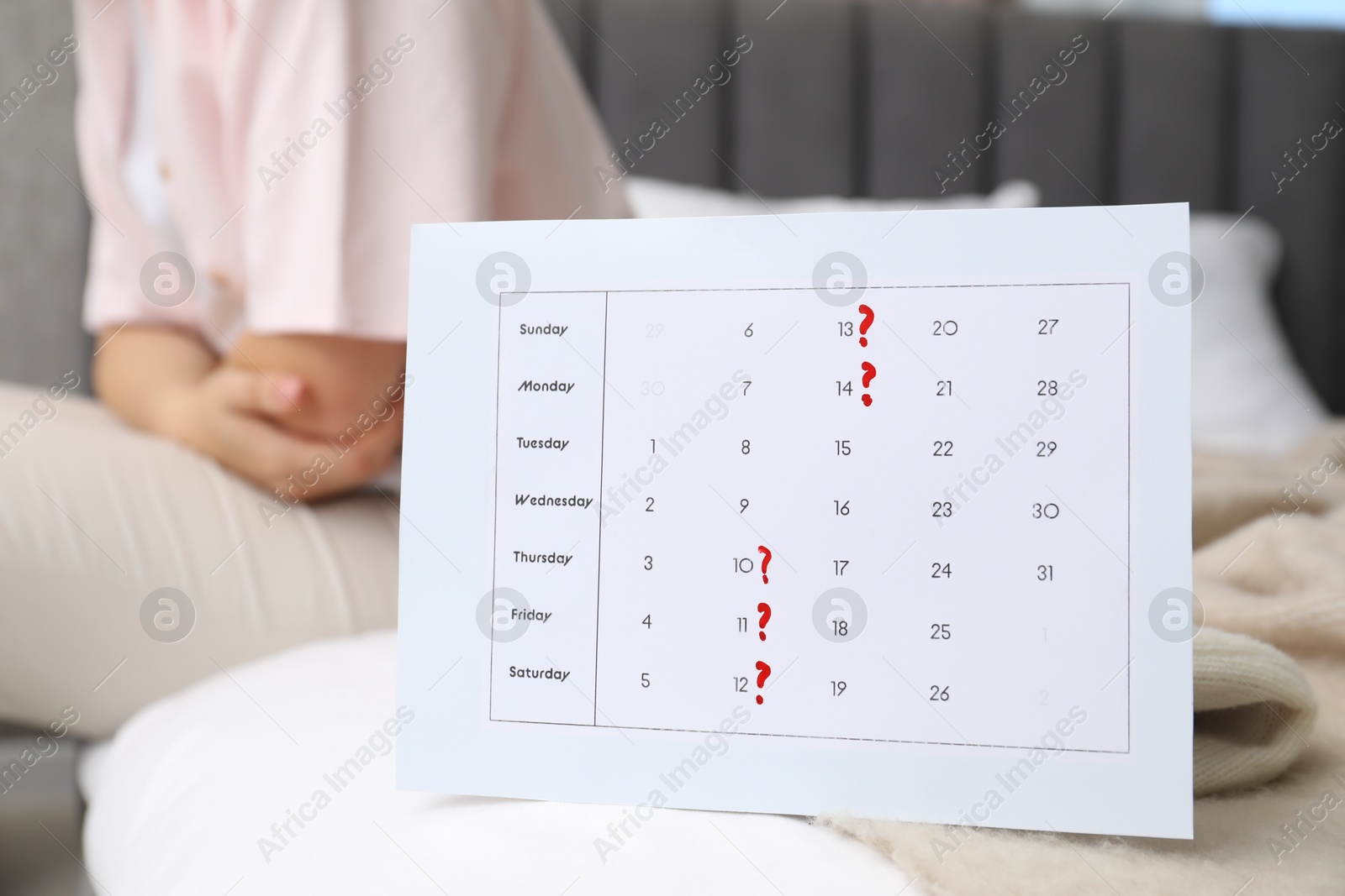 Photo of Woman suffering from abdominal pain in bed at home, focus on calendar with marked menstrual cycle days