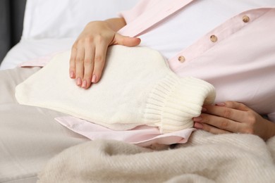 Photo of Woman using hot water bottle to relieve menstrual pain on bed at home, closeup