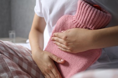 Woman using hot water bottle to relieve menstrual pain at home, closeup