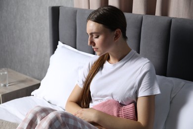 Woman using hot water bottle to relieve menstrual pain on bed at home