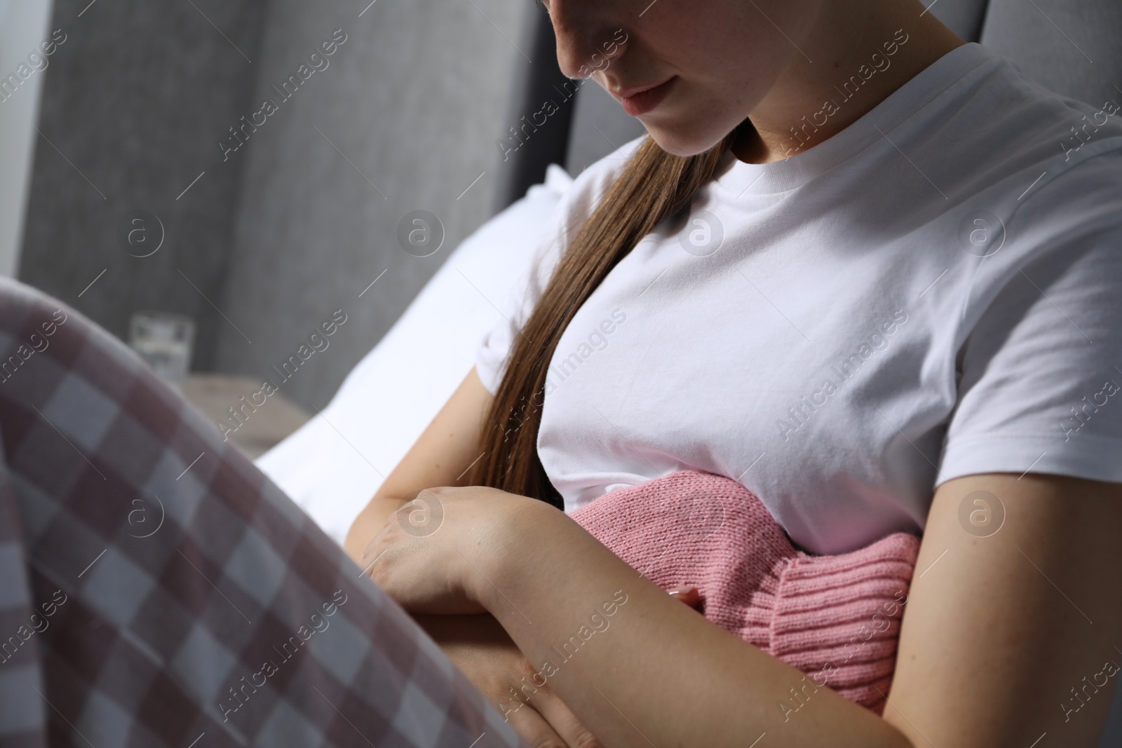 Photo of Woman using hot water bottle to relieve menstrual pain at home, closeup