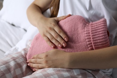 Woman using hot water bottle to relieve menstrual pain on bed at home, closeup