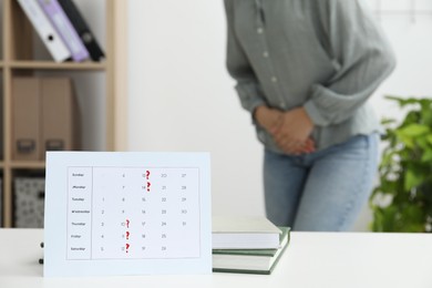 Photo of Woman suffering from abdominal pain indoors, focus on calendar with marked menstrual cycle days