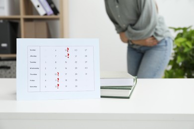 Photo of Woman suffering from abdominal pain indoors, focus on calendar with marked menstrual cycle days