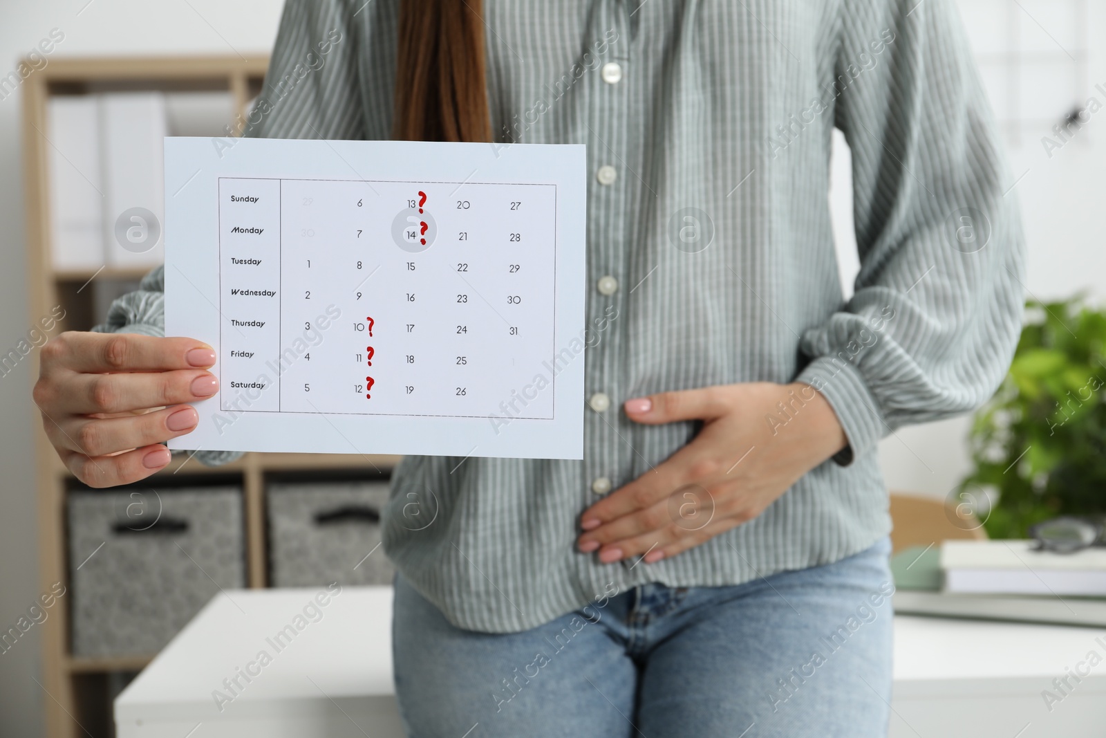 Photo of Woman holding calendar with marked menstrual cycle days and suffering from abdominal pain indoors, closeup