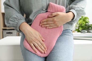 Woman using hot water bottle to relieve menstrual pain indoors, closeup