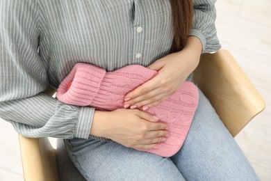 Woman using hot water bottle to relieve menstrual pain indoors, closeup