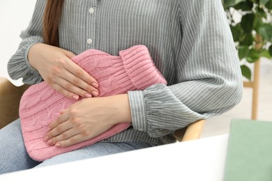 Woman using hot water bottle to relieve menstrual pain indoors, closeup