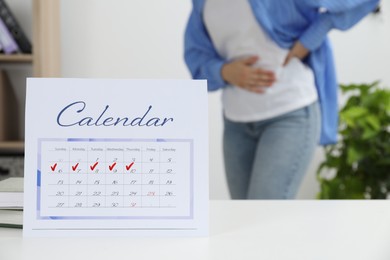 Photo of Woman suffering from abdominal pain indoors, focus on calendar with marked menstrual cycle days