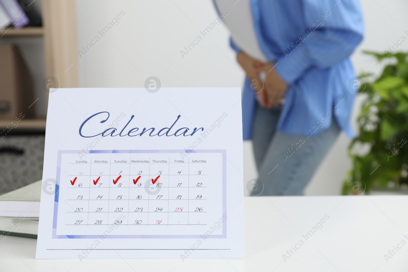 Photo of Woman suffering from abdominal pain indoors, focus on calendar with marked menstrual cycle days