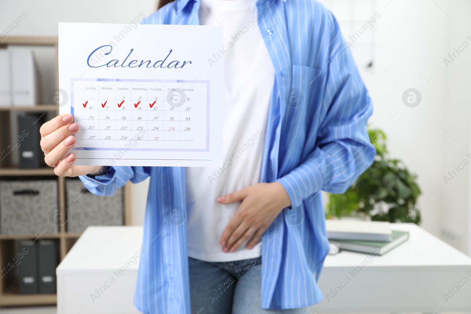 Photo of Woman holding calendar with marked menstrual cycle days and suffering from abdominal pain indoors, closeup