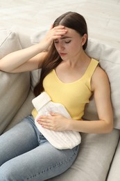 Woman using hot water bottle to relieve menstrual pain on sofa at home