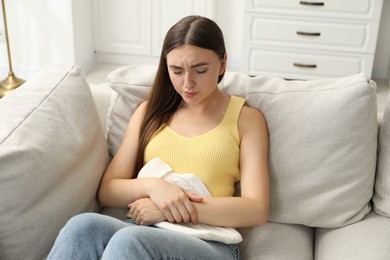 Photo of Woman using hot water bottle to relieve menstrual pain on sofa at home