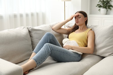 Photo of Woman using hot water bottle to relieve menstrual pain on sofa at home