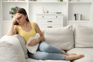 Photo of Woman using hot water bottle to relieve menstrual pain on sofa at home