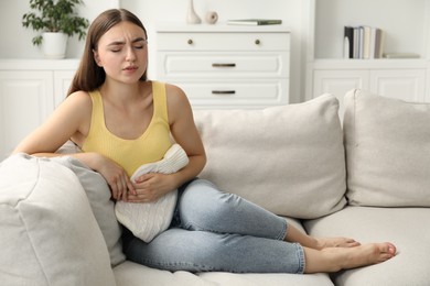 Photo of Woman using hot water bottle to relieve menstrual pain on sofa at home