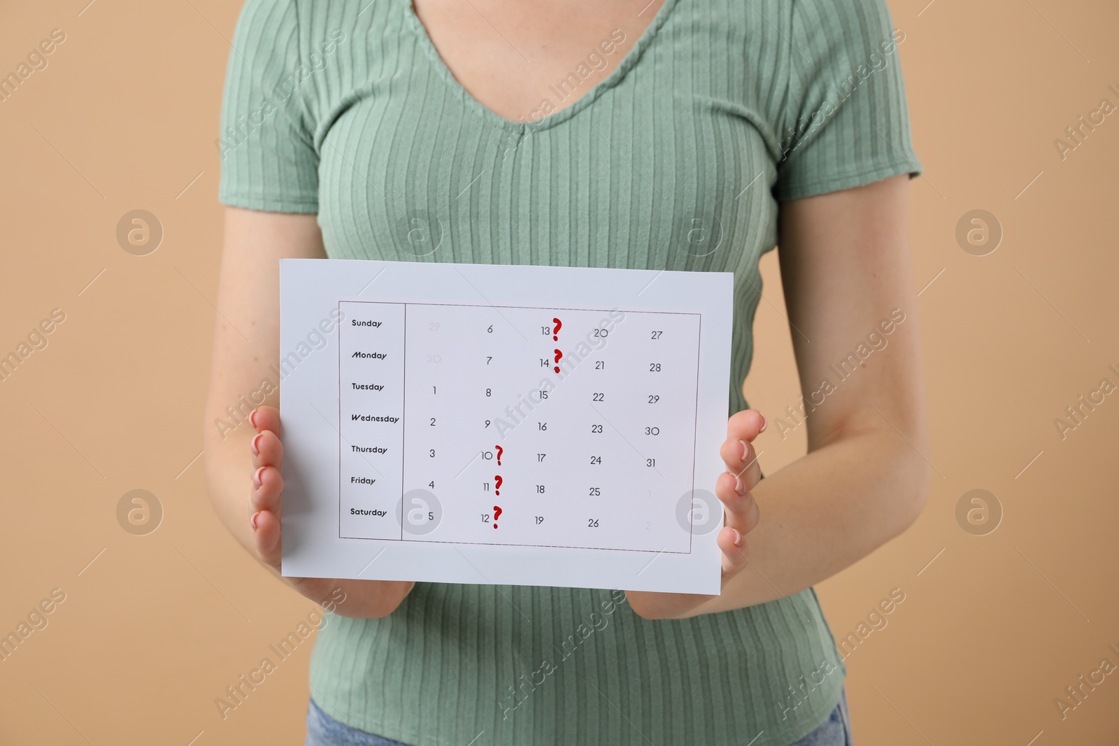 Photo of Woman holding calendar with marked menstrual cycle days on beige background, closeup