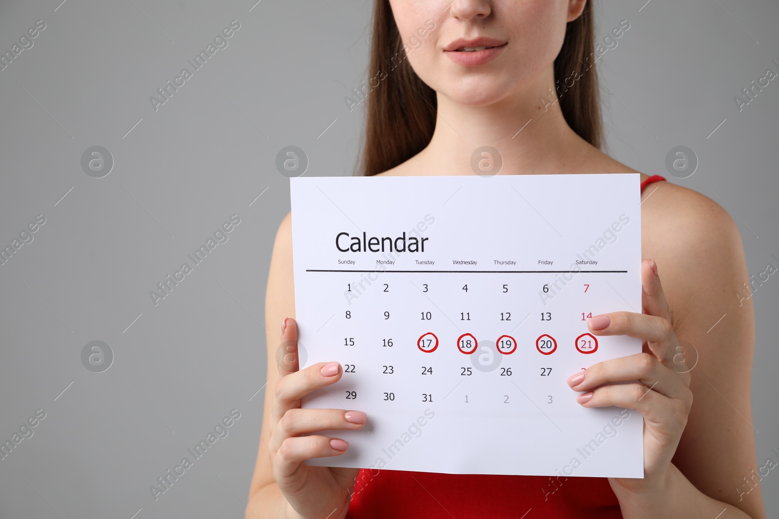 Photo of Woman holding calendar with marked menstrual cycle days on grey background, closeup. Space for text