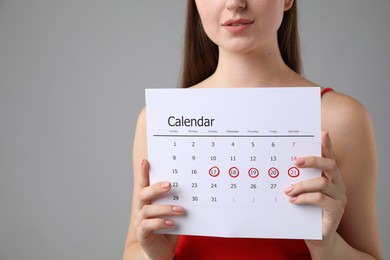 Woman holding calendar with marked menstrual cycle days on grey background, closeup. Space for text