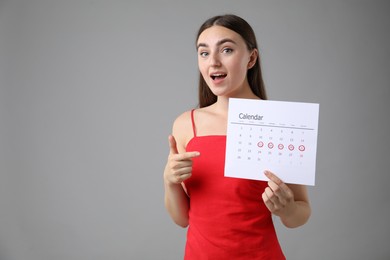 Photo of Woman holding calendar with marked menstrual cycle days on grey background, space for text