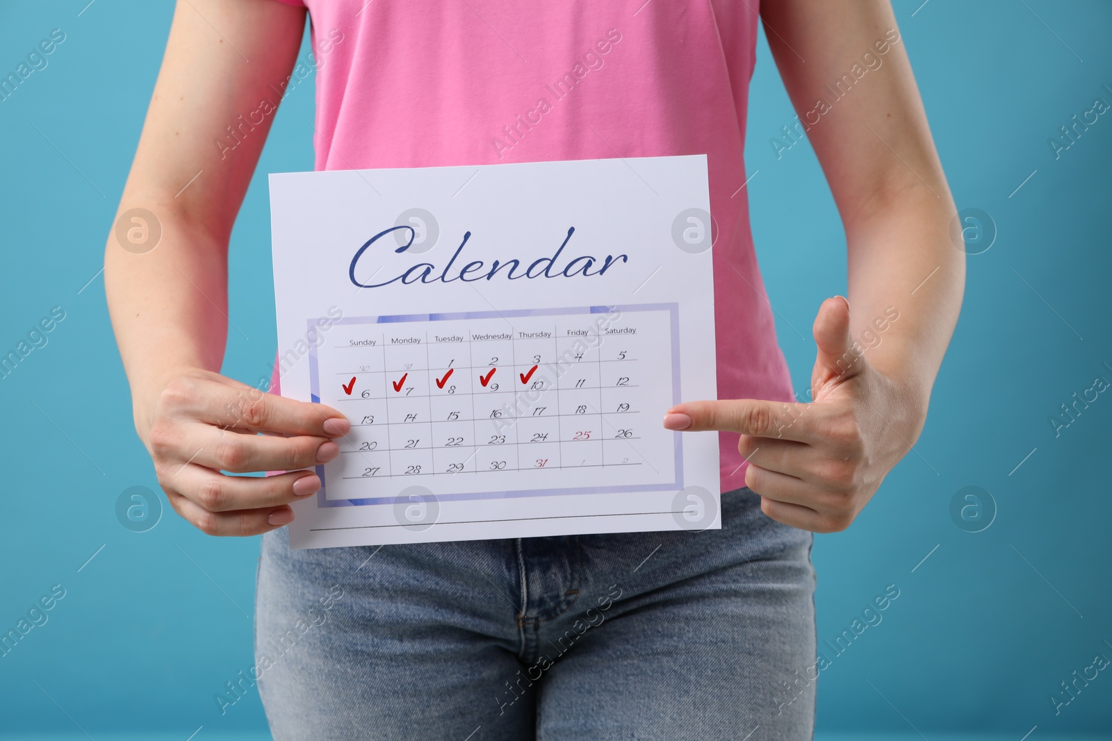 Photo of Woman holding calendar with marked menstrual cycle days on light blue background, closeup