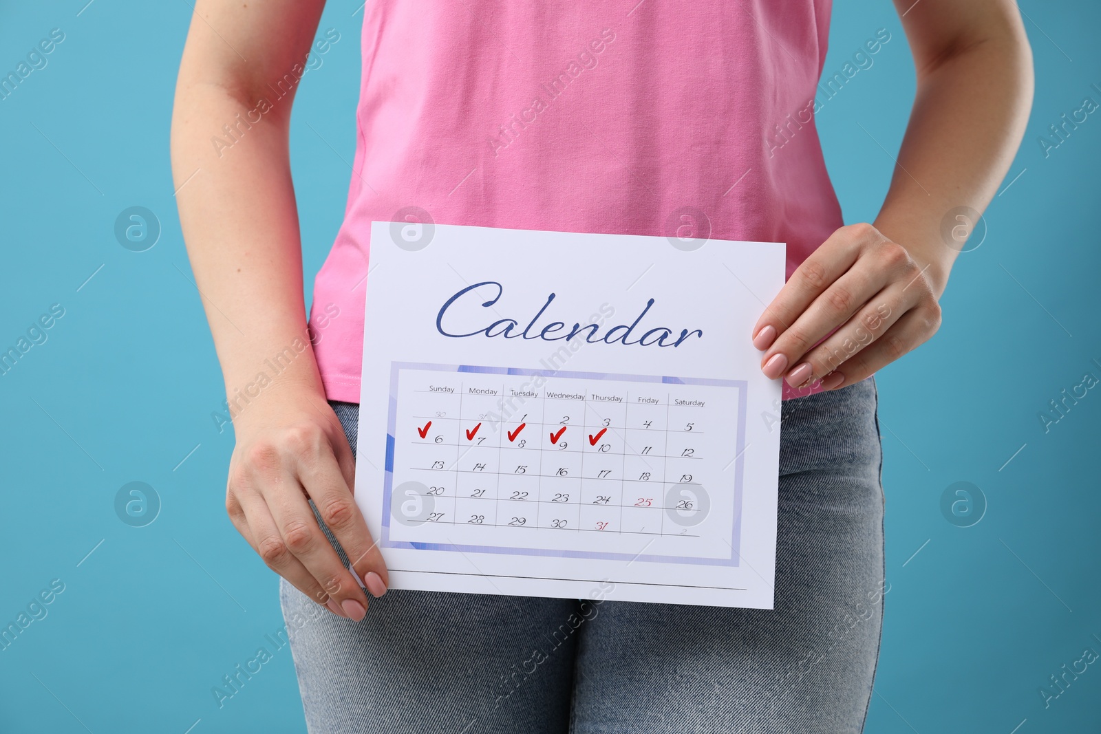 Photo of Woman holding calendar with marked menstrual cycle days on light blue background, closeup