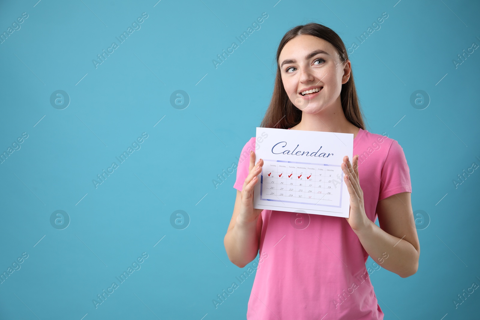 Photo of Woman holding calendar with marked menstrual cycle days on light blue background, space for text