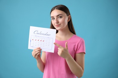 Woman holding calendar with marked menstrual cycle days on light blue background