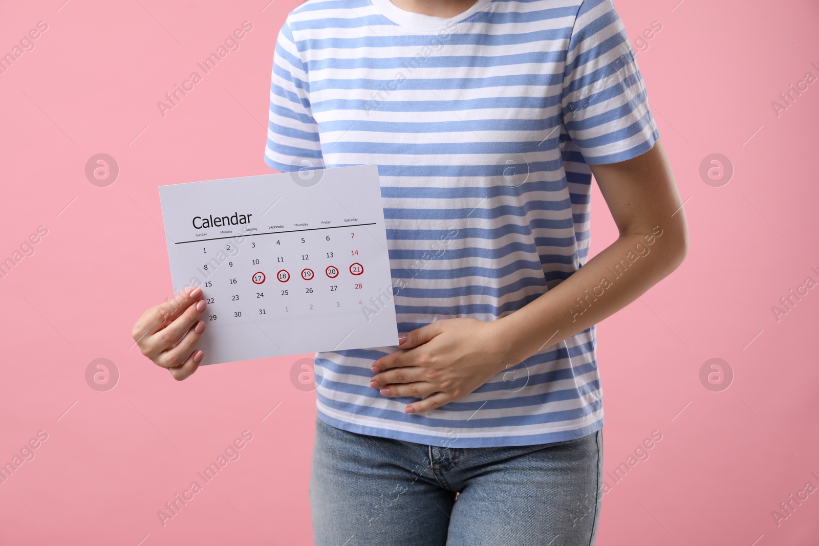 Photo of Woman holding calendar with marked menstrual cycle days and suffering from abdominal pain on pink background, closeup