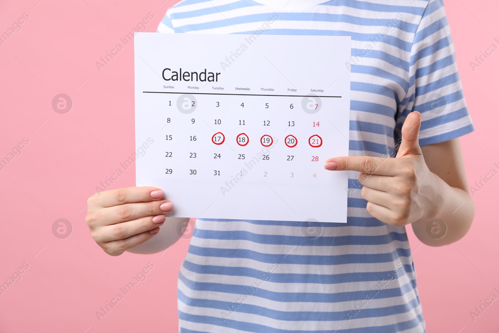 Photo of Woman holding calendar with marked menstrual cycle days on pink background, closeup