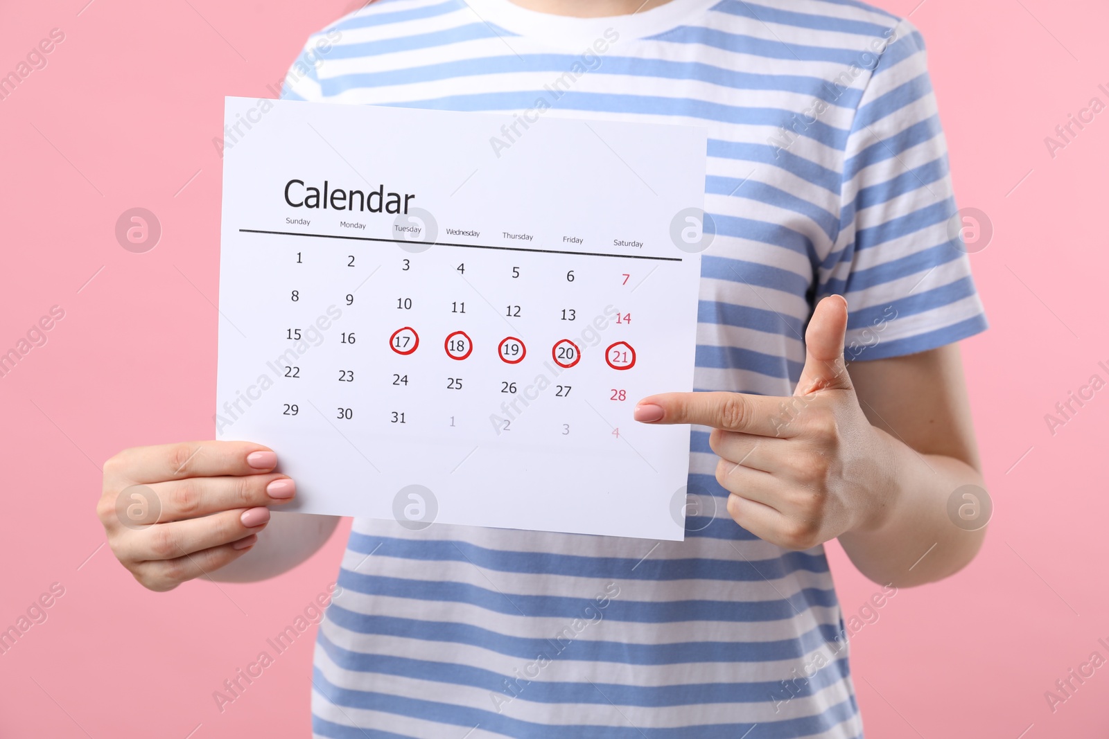 Photo of Woman holding calendar with marked menstrual cycle days on pink background, closeup