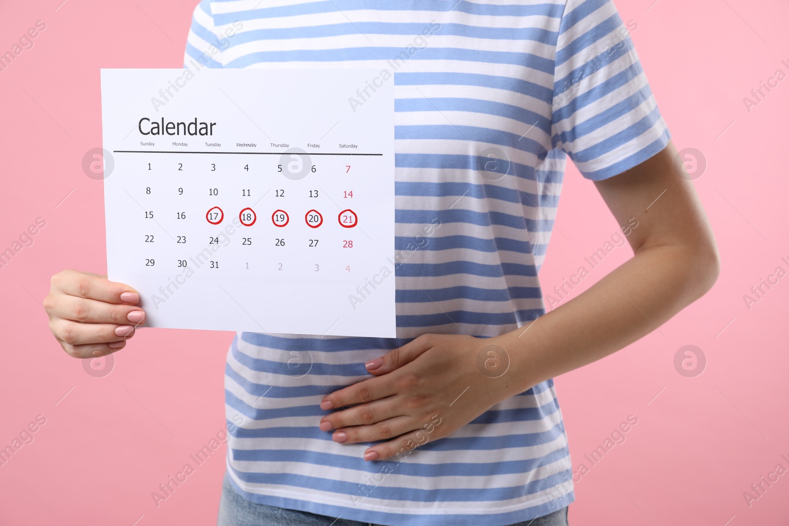 Photo of Woman holding calendar with marked menstrual cycle days and suffering from abdominal pain on pink background, closeup