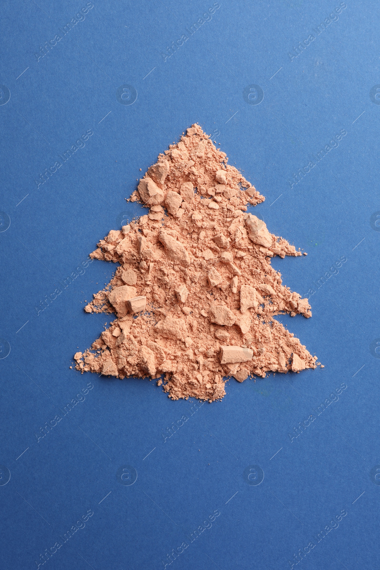 Photo of Christmas tree made with face powder on blue background, top view